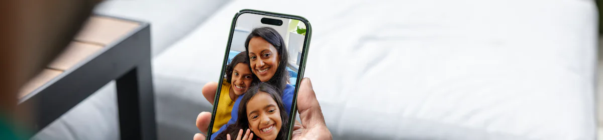 Over the shoulder view of a man watching an Evri video on his mobile phone. The video is of a mother and two children waving and smiling.