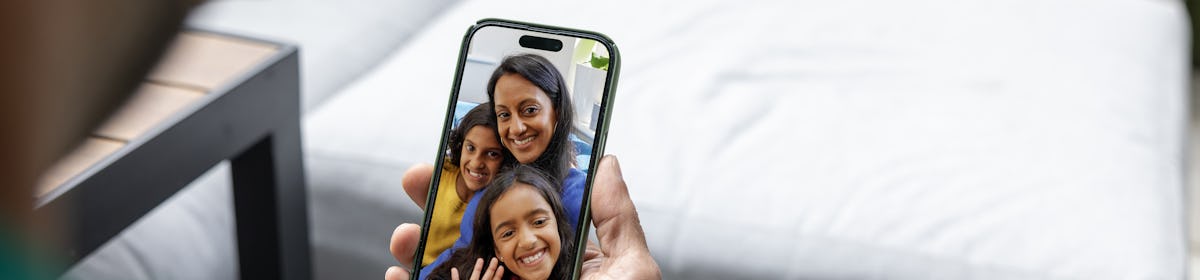 Over the shoulder view of a man watching an Evri video on his mobile phone. The video is of a mother and two children waving and smiling.