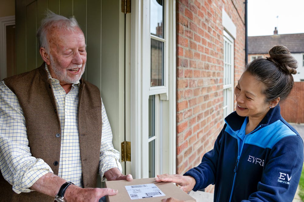 A handful of parcels are being handed to a recipient at the door. Both the courier and recipient are clearly visible
