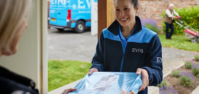 A parcel in waterproof blue packaging is being handed to a recipient at the door. A blue Evri van can be seen in the background.
