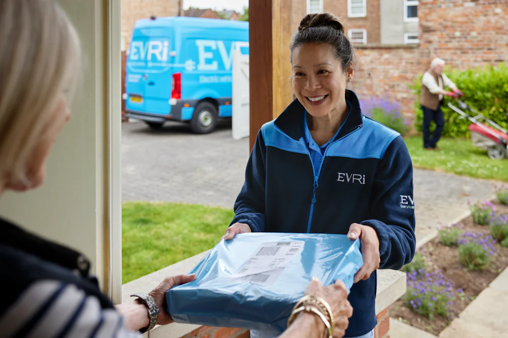 A parcel in waterproof blue packaging is being handed to a recipient at the door. A blue Evri van can be seen in the background.