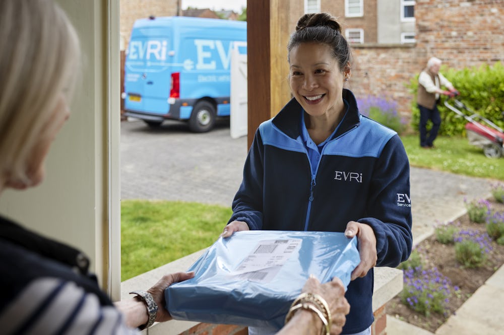 A parcel in waterproof blue packaging is being handed to a recipient at the door. A blue Evri van can be seen in the background.