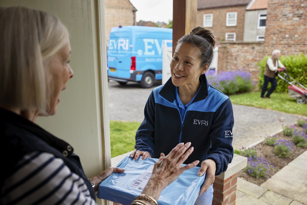 A parcel in waterproof blue packaging is being handed to a recipient at the door. A blue Evri van can be seen in the background.