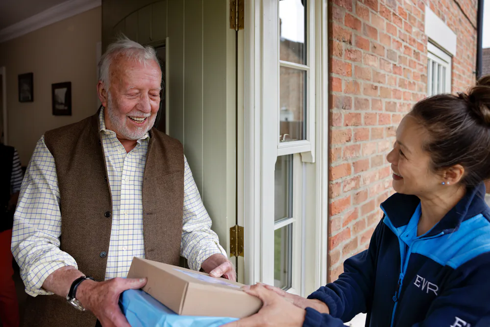 A handful of parcels are being handed to a recipient at the door. Both the courier and recipient are clearly visible