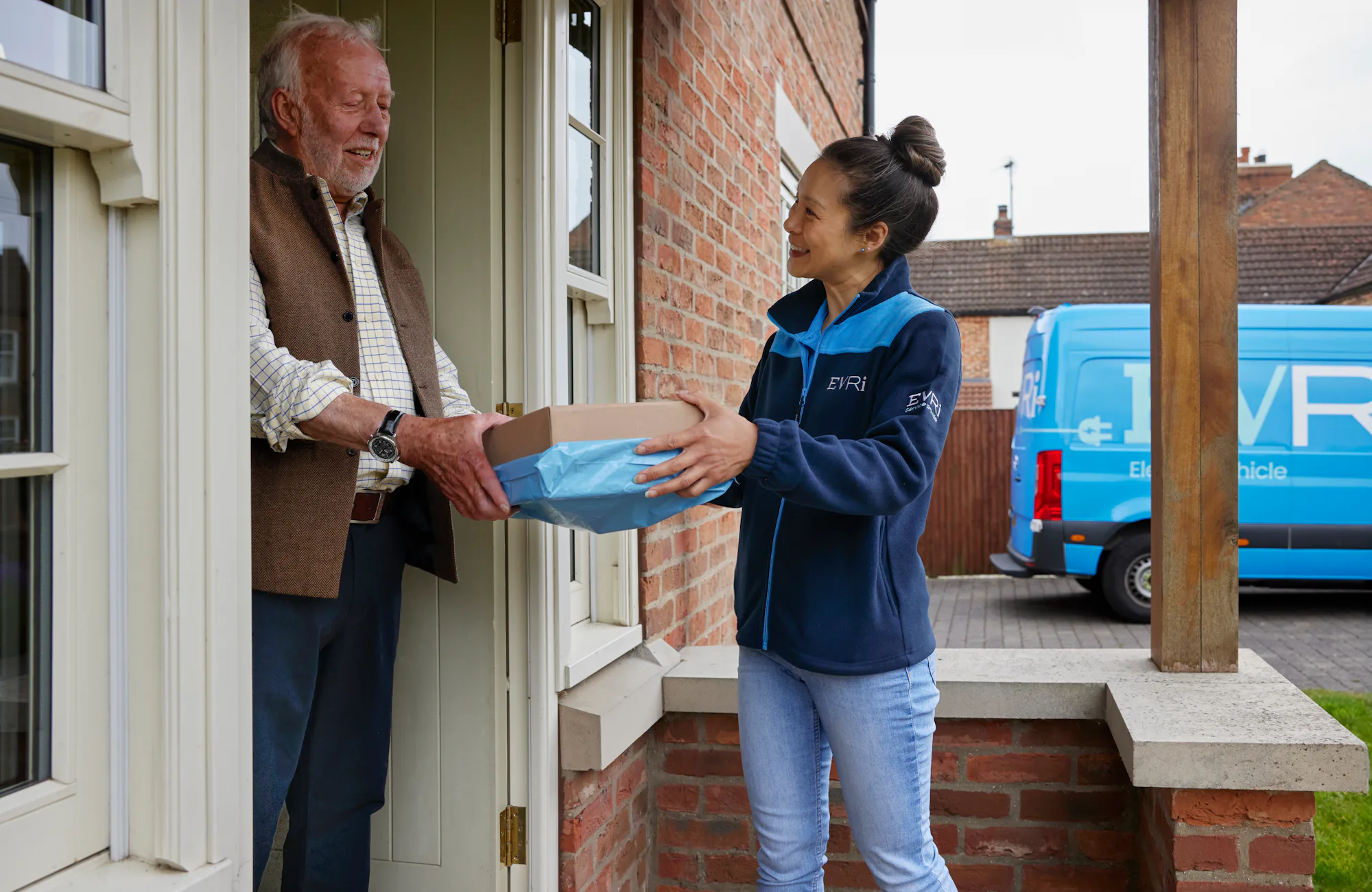 A handful of parcels are being handed to a recipient at the door. Both the courier and recipient are clearly visible