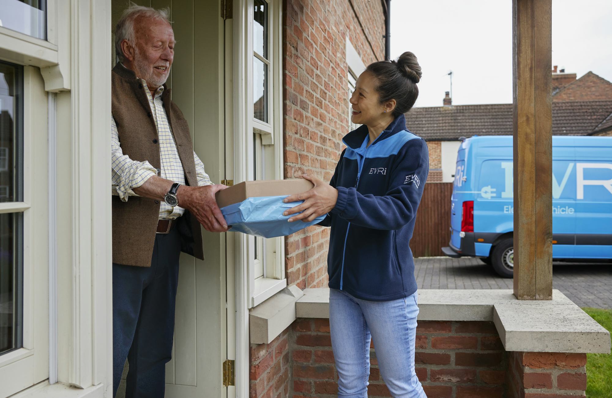 A handful of parcels are being handed to a recipient at the door. Both the courier and recipient are clearly visible