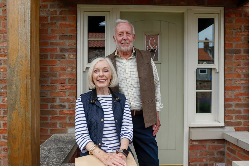 An older couple pose on their doorstep with their parcel after an Evri delivery.