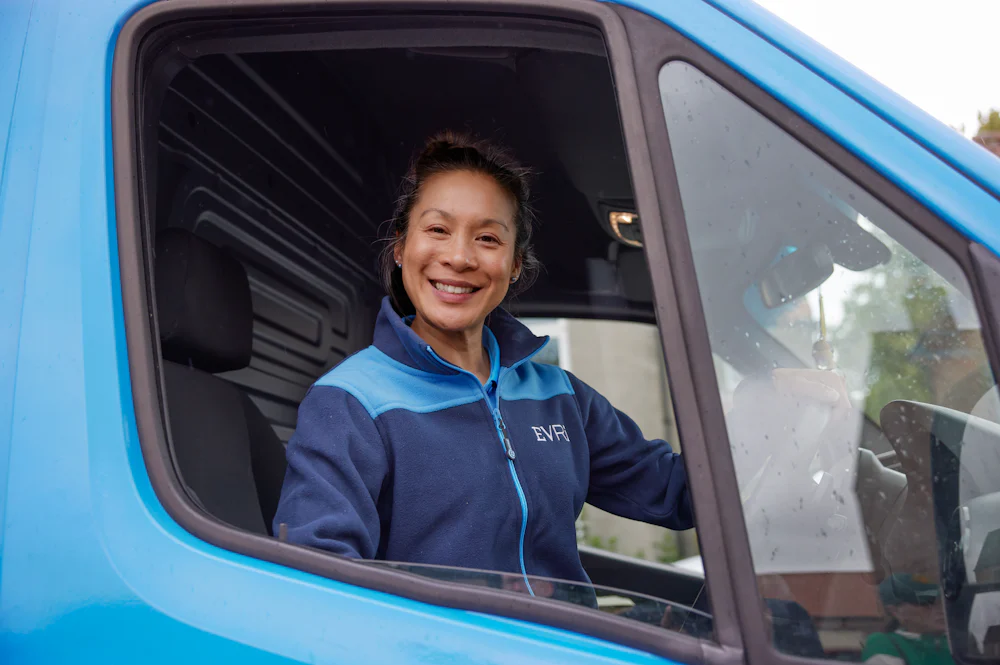 A female Evri van driver poses in the driving seat of her blue Evri van.