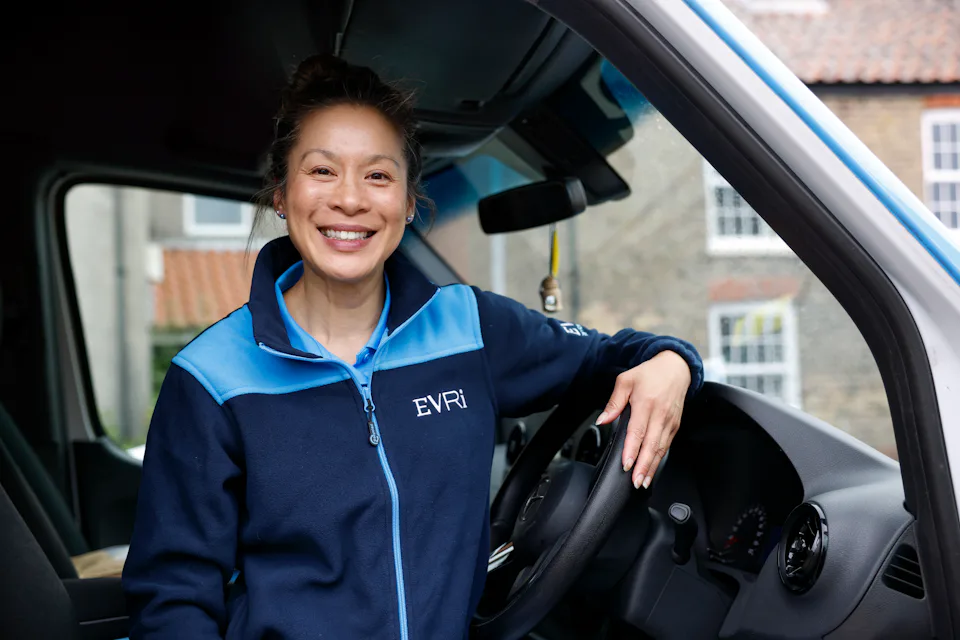 A female Evri van driver poses in the driving seat of her blue Evri van.