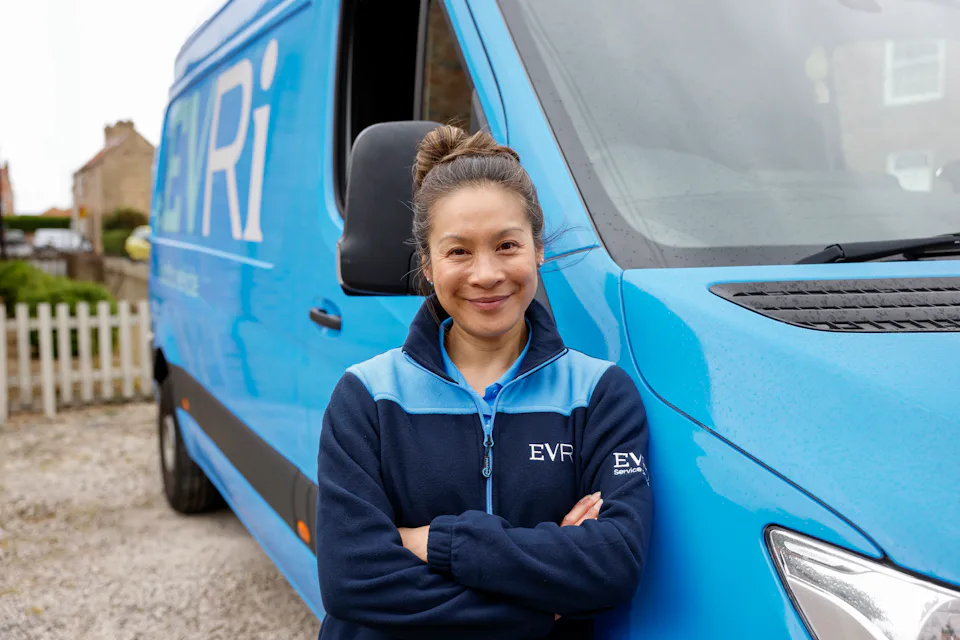 A female Evri van driver poses in front of her blue Evri van.