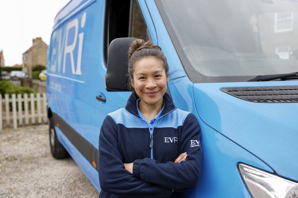 A female Evri van driver poses in front of her blue Evri van.