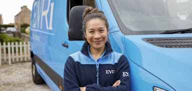 A female Evri van driver poses in front of her blue Evri van.