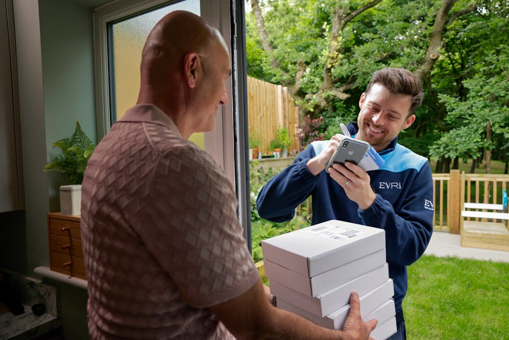 An Evri Courier leaving a stack of parcels with a neighbour due to the recipient not being in. He is taking the name of the neighbour on a blue slip to post to the recipient.