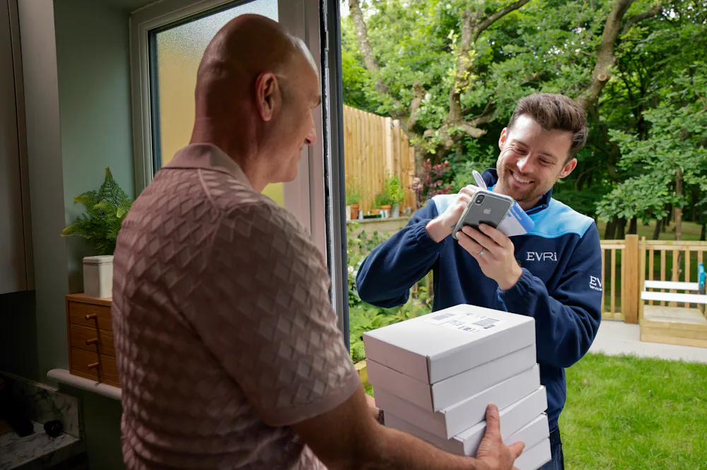 An Evri Courier leaving a stack of parcels with a neighbour due to the recipient not being in. He is taking the name of the neighbour on a blue slip to post to the recipient.