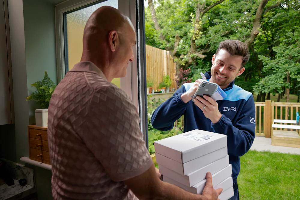 An Evri Courier leaving a stack of parcels with a neighbour due to the recipient not being in. He is taking the name of the neighbour on a blue slip to post to the recipient.