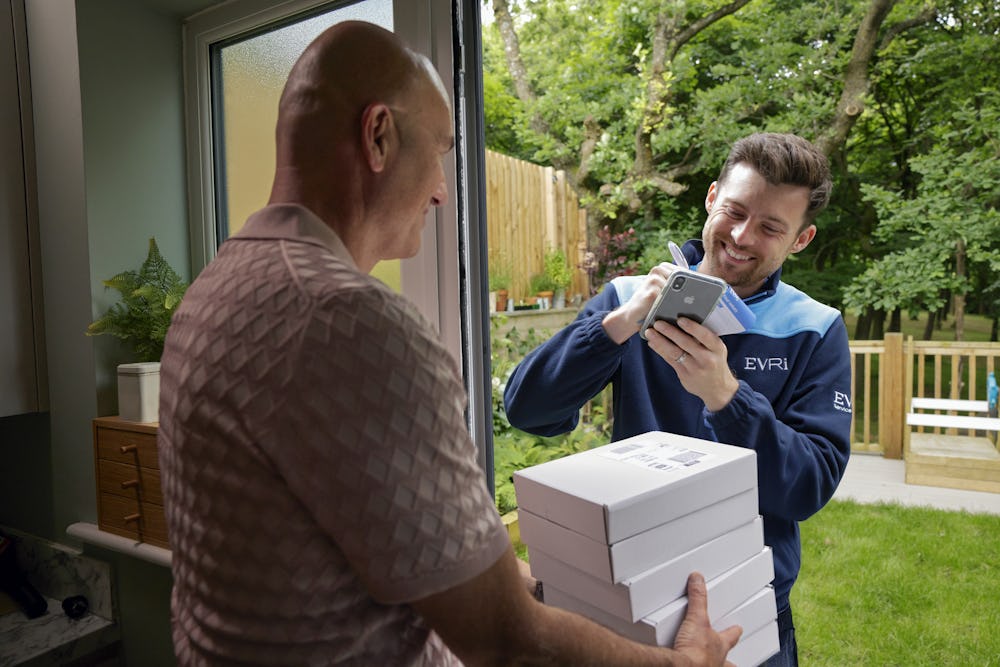An Evri Courier leaving a stack of parcels with a neighbour due to the recipient not being in. He is taking the name of the neighbour on a blue slip to post to the recipient.