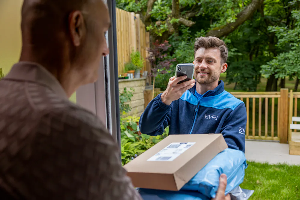 An Evri courier is taking a photo confirmation of a successful delivery whilst the customer holds the parcels in clear view.