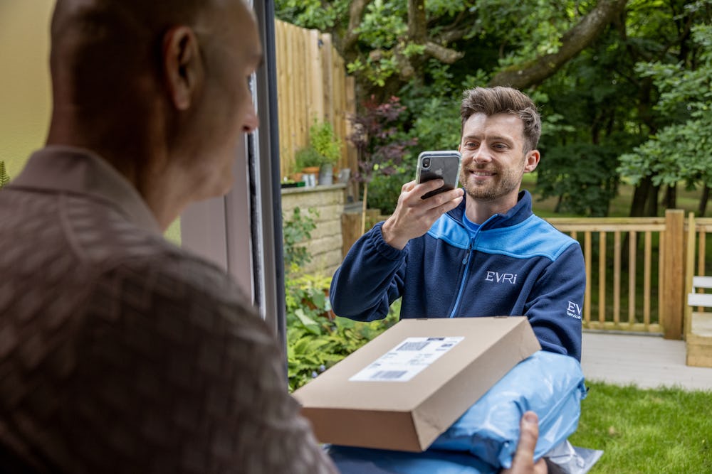 An Evri courier is taking a photo confirmation of a successful delivery whilst the customer holds the parcels in clear view.