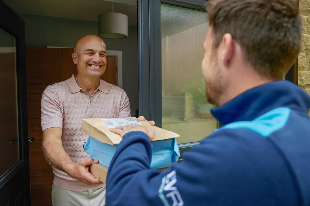 An Evri courier is handing three parcels to a man at his doorstep. They are both laughing as if a funny joke or anecdote was shared.