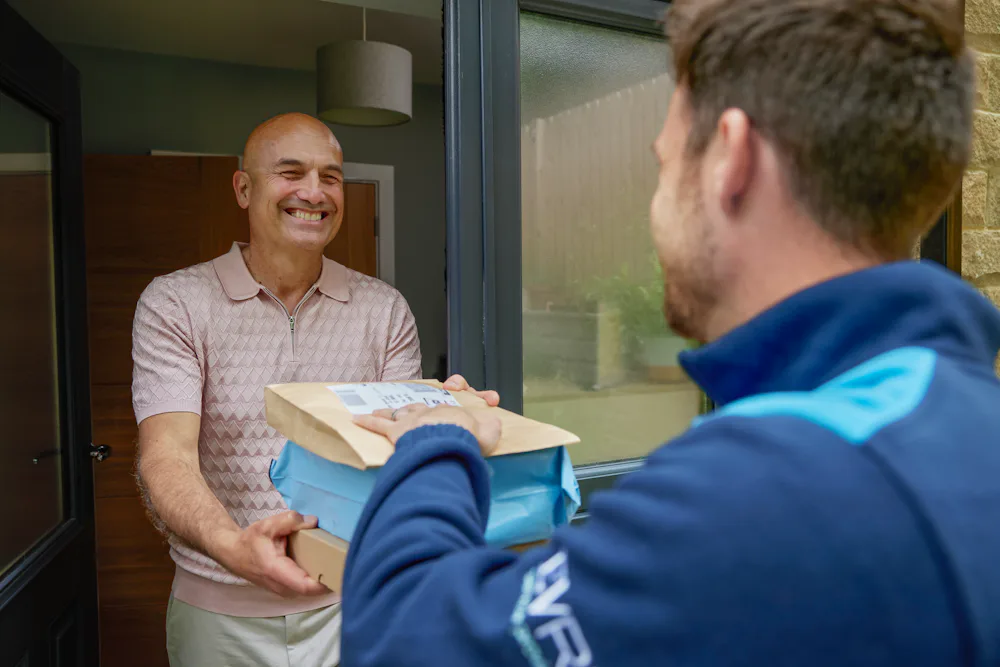 An Evri courier is handing three parcels to a man at his doorstep. They are both laughing as if a funny joke or anecdote was shared.
