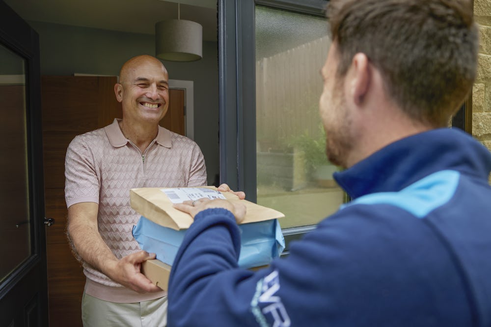 An Evri courier is handing three parcels to a man at his doorstep. They are both laughing as if a funny joke or anecdote was shared.