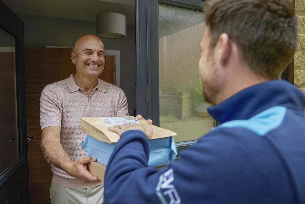 An Evri courier is handing three parcels to a man at his doorstep. They are both laughing as if a funny joke or anecdote was shared.
