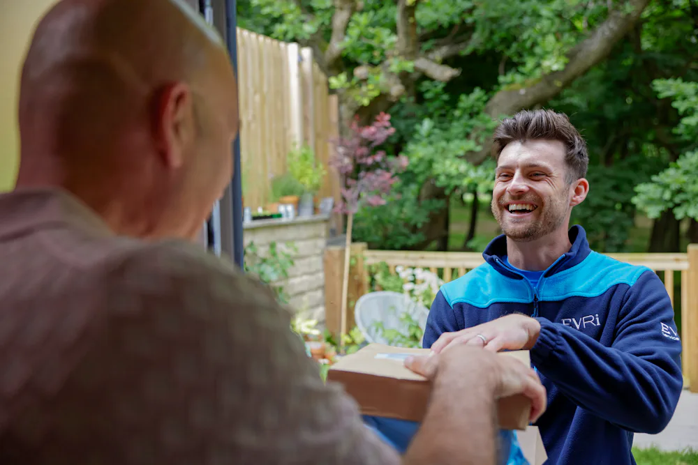An Evri courier is handing three parcels to a man at his doorstep. They are both laughing as if a funny joke or anecdote was shared.