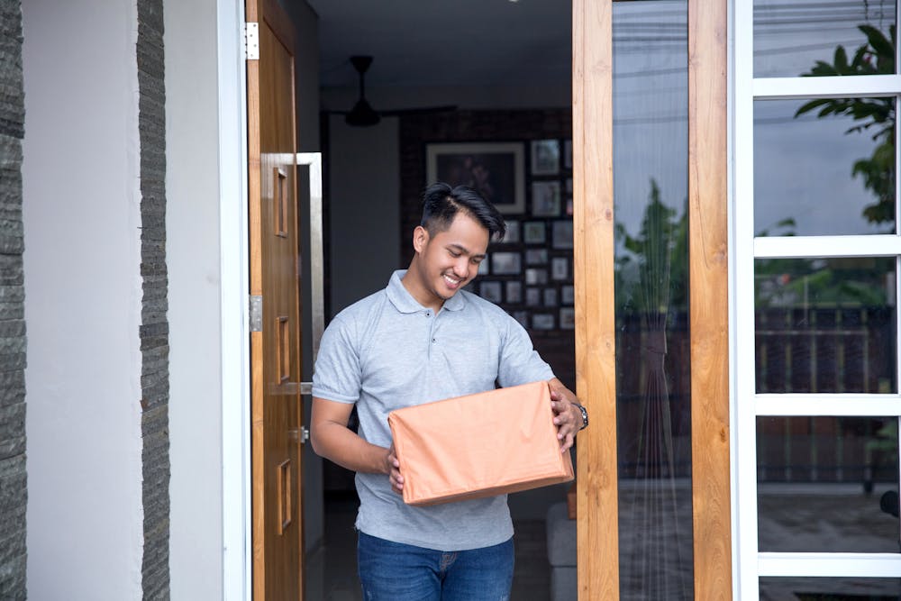 A customer is standing in their doorway holding a large parcel and looking down at it with a smile.