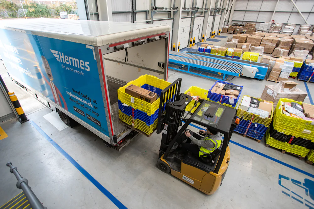 An Evri truck being loaded with palettes full of parcels by a forklift. The truck is docked in a large fufilment hub