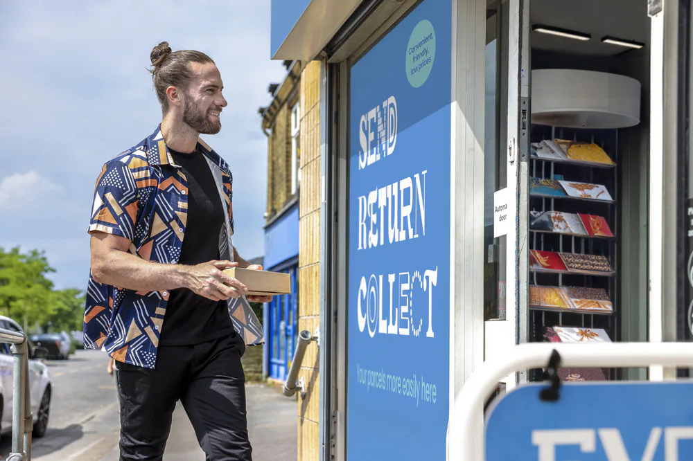 Customer stood outside of a ParcelShop store smiling and holding a parcel. The blue Evri signage can be seen on the storefront.