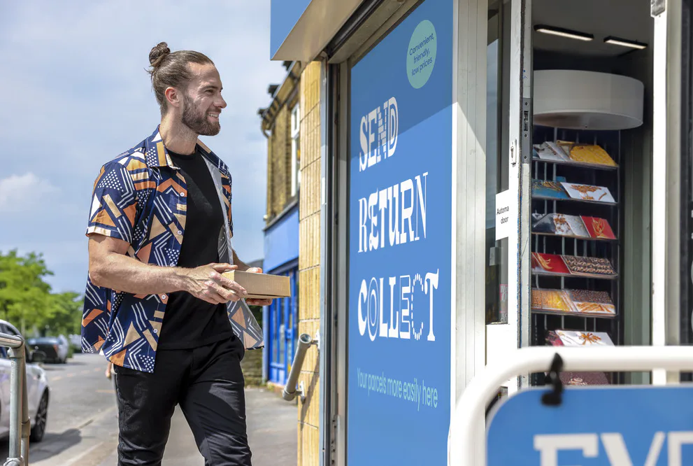 Customer stood outside of a ParcelShop store smiling and holding a parcel. The blue Evri signage can be seen on the storefront.