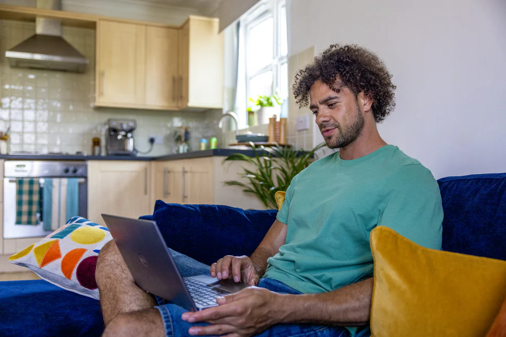 A side-view profile of a customer sitting on a sofa, with a laptop resting on their lap as they look down at the screen.