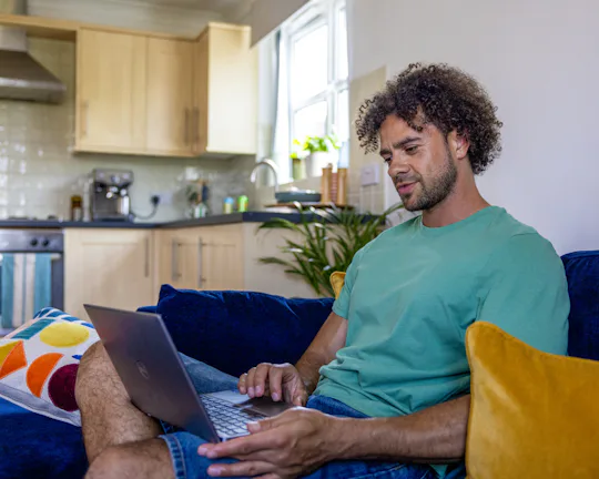 A side-view profile of a customer sitting on a sofa, with a laptop resting on their lap as they look down at the screen.