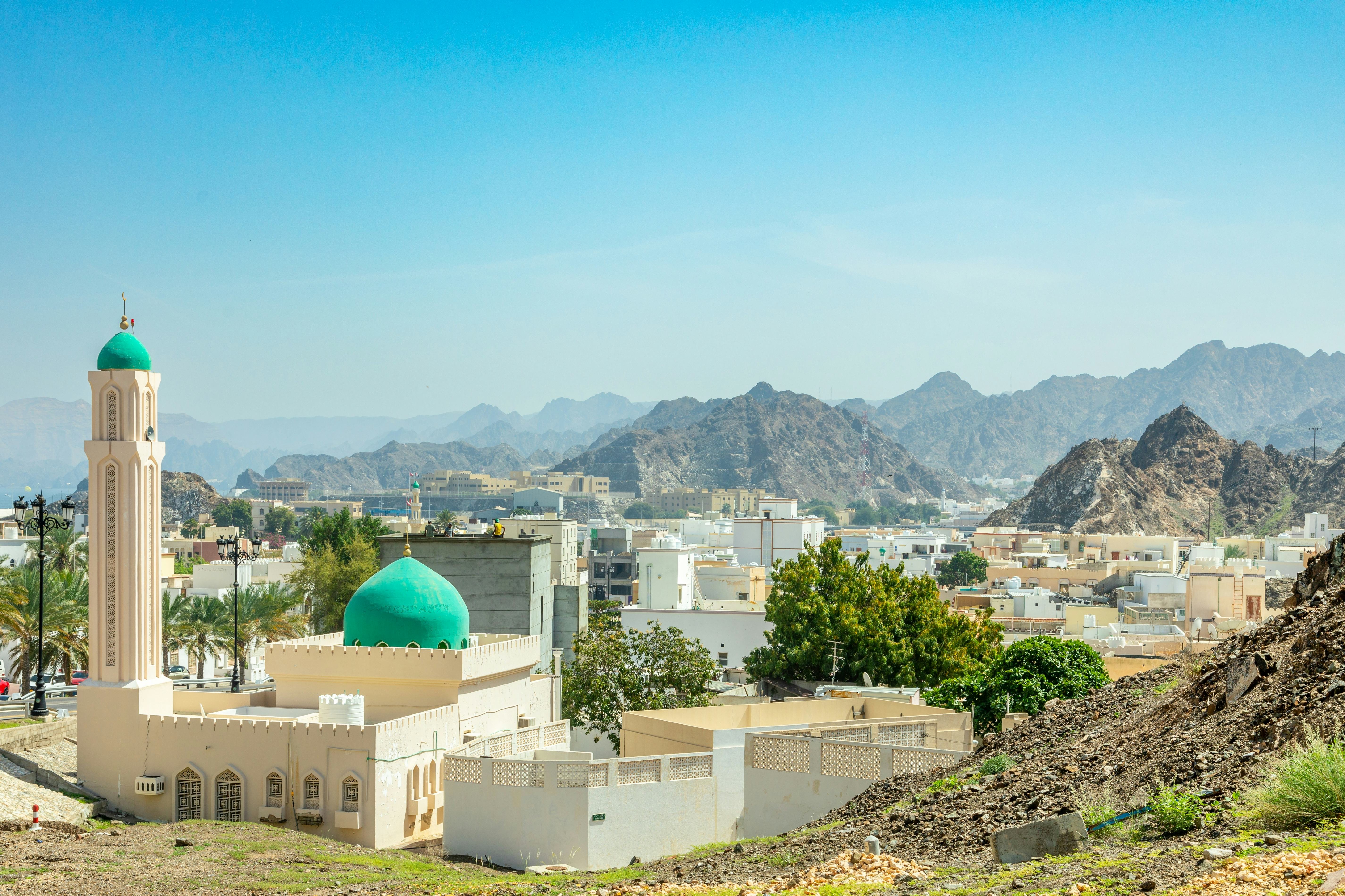 A skyline view of Oman with a mosque and buildings in a rocky, mountainous landscape.