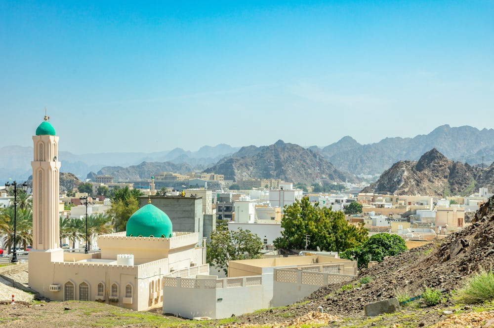 A skyline view of Oman with a mosque and buildings in a rocky, mountainous landscape.