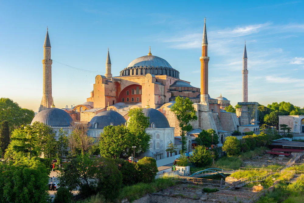 A landscape photo showing the Hagia Sophia Grand Mosque in Turkey surrounded by trees and blue sky.