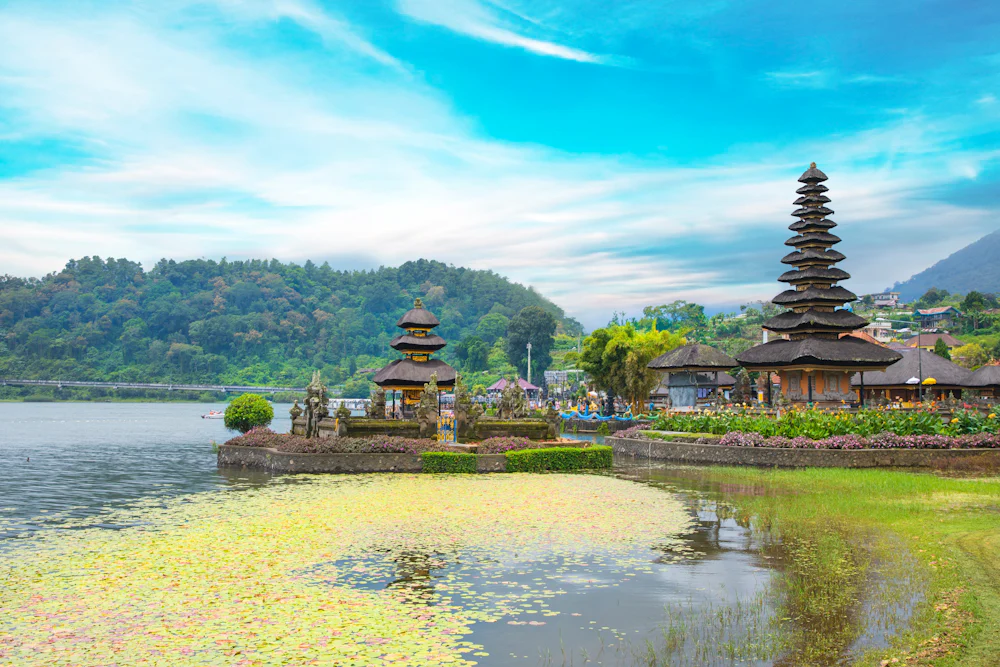 A landscape photo capturing a temple in Indonesia by a lake and surrounded by tree-covered mountains