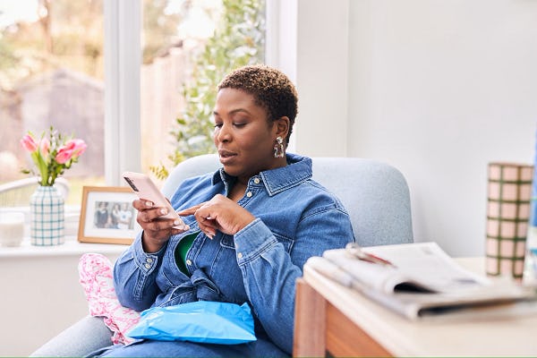 woman sat on armchair with package in knee and smartphone in hand