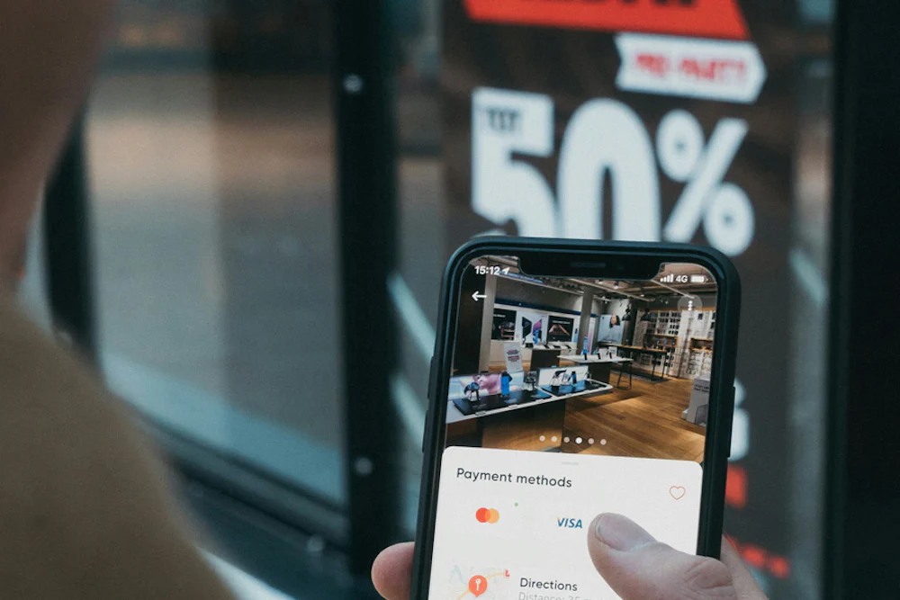 A customer holding their mobile phone with a large Black Friday sale sign in the window of a shop visible in the background