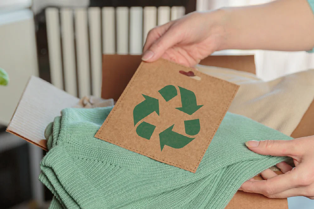 A close-up of a business owner packaging an item of clothing and holding a recyclable symbol to show sustainability of their product and/or packaging