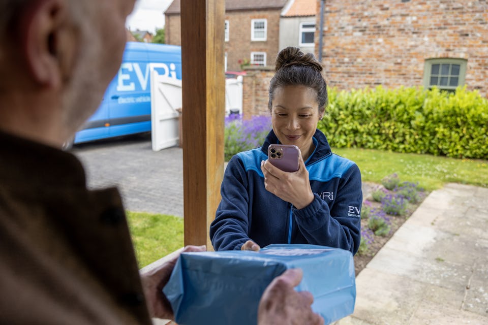 Evri courier delivers and scans a parcel for a customer who is accepting the parcel on their doorstep