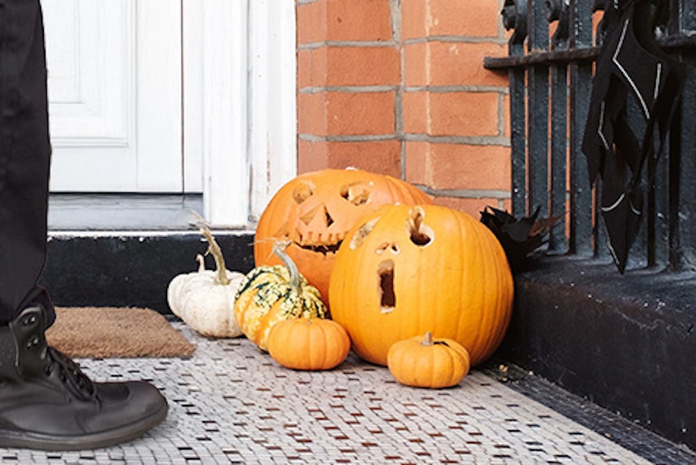 A courier standing on the doorstep, holding a parcel to deliver, with carved pumpkins by their feet.