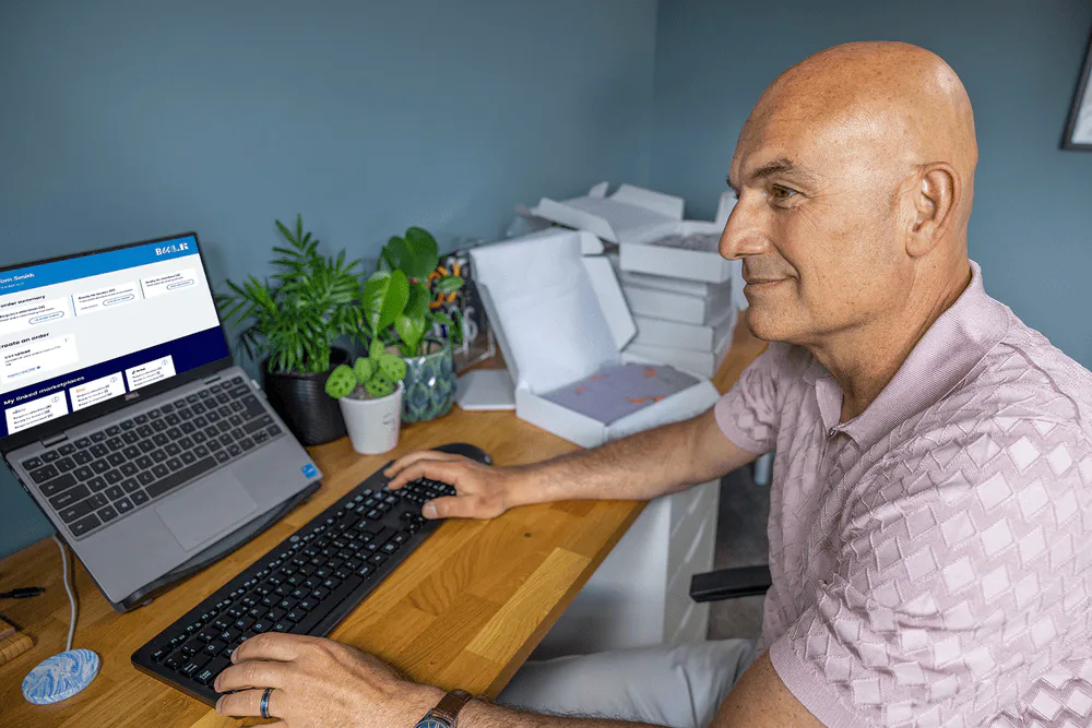 Business owner sat at a desk in their home office using their laptop to book multiple parcels