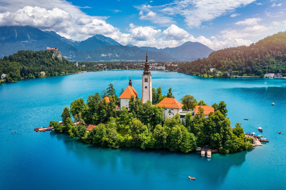 A landscape view of an island in a vivid blue lake with a church and red-roofed buildings in Slovenia.
