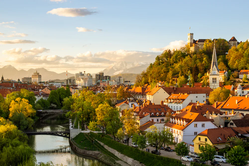 A landscape view of a red-roofed town in Slovenia by a river and peppered with green trees.