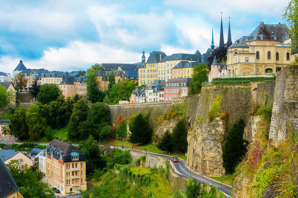 A landscape view of a road lining a rocky sheer cliff edge with buildings on either side in Luxembourg