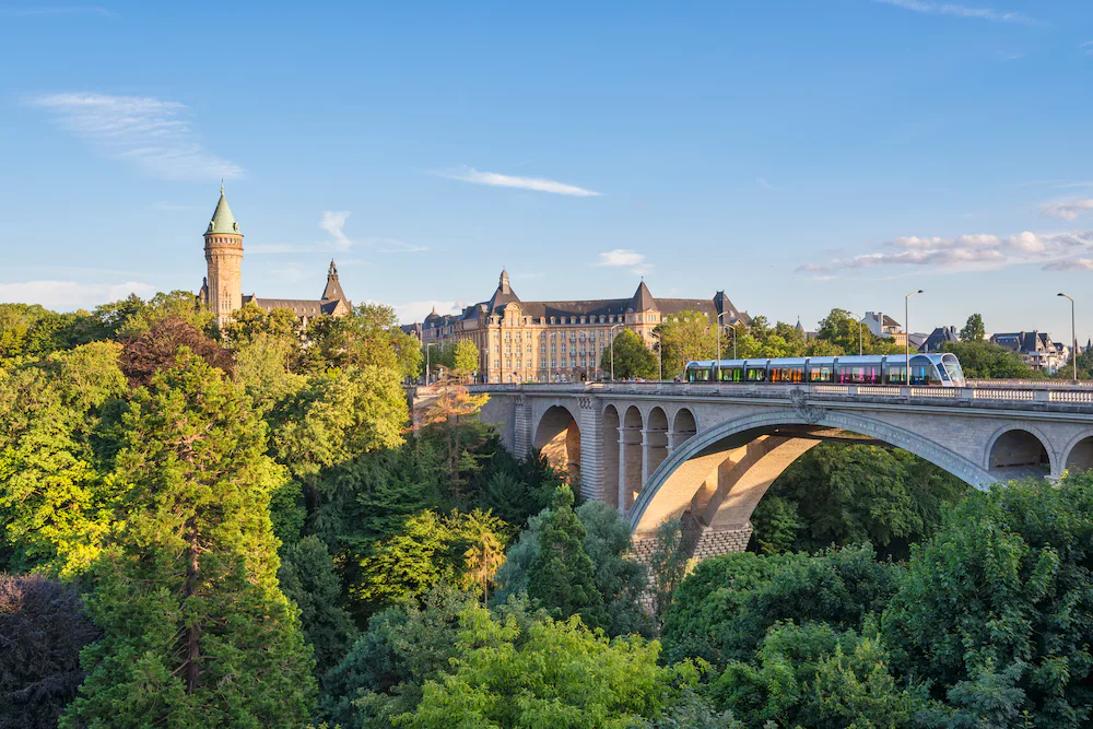 A landscape view of a bridge crossing a valley in Luxembourg with a train crossing and lots of tree foliage.
