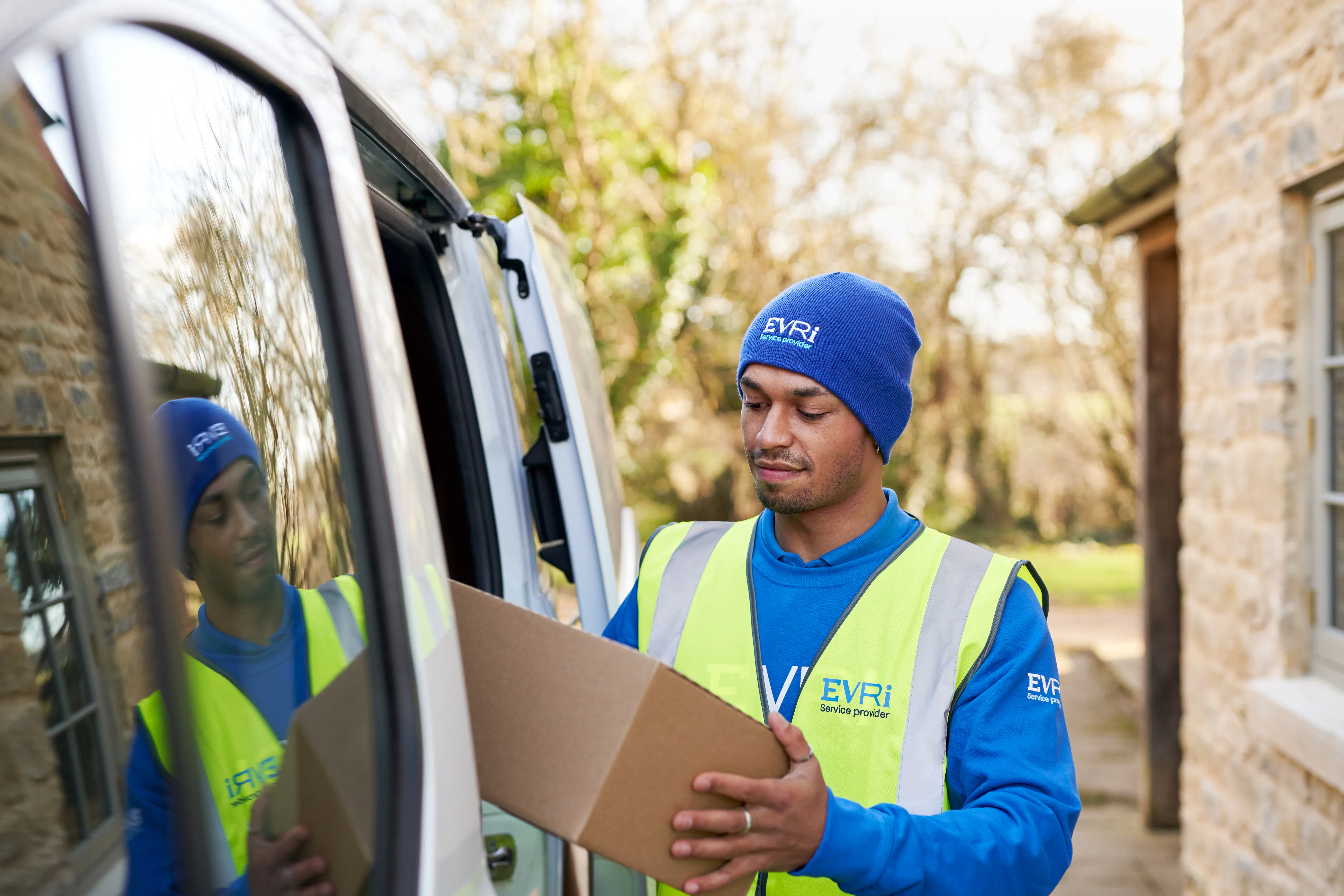 courier opening door of white van and placing cardboard box inside