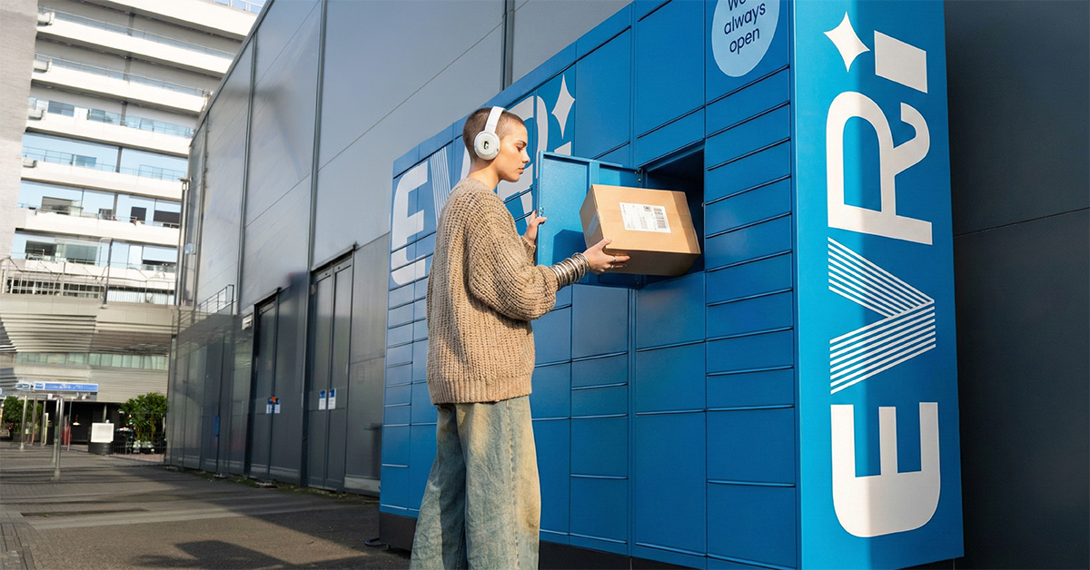 A person wearing headphones places a parcel into a blue Evri Locker unit outside a modern building in an urban area.