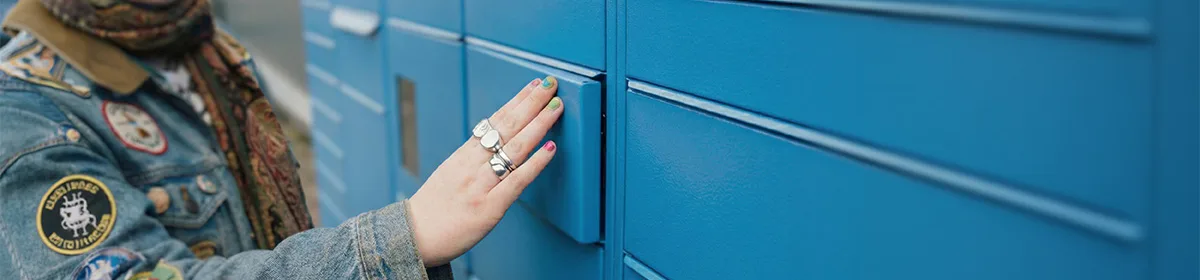 A smiling person wearing a denim jacket and a beanie presses a compartment door on a blue Evri Locker unit.